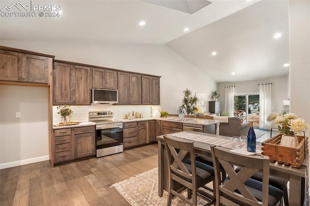 kitchen featuring sink, stainless steel appliances, tasteful backsplash, light hardwood / wood-style flooring, and high vaulted ceiling