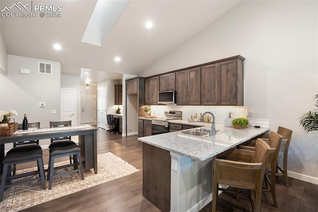 kitchen with kitchen peninsula, vaulted ceiling with skylight, stainless steel appliances, sink, and dark hardwood / wood-style floors