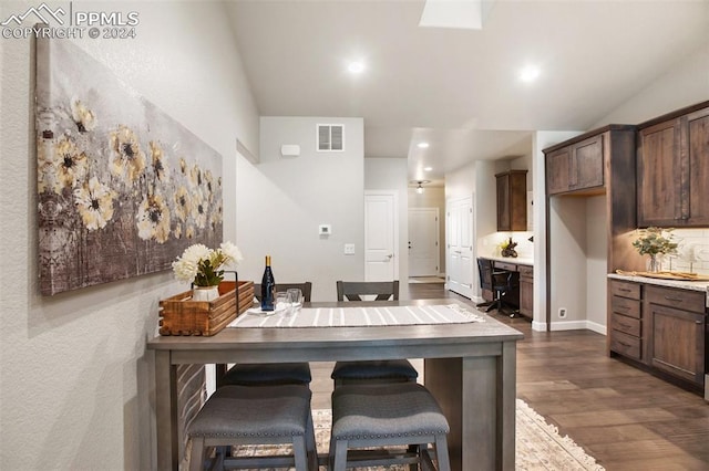 kitchen featuring a kitchen bar, dark brown cabinetry, and dark wood-type flooring