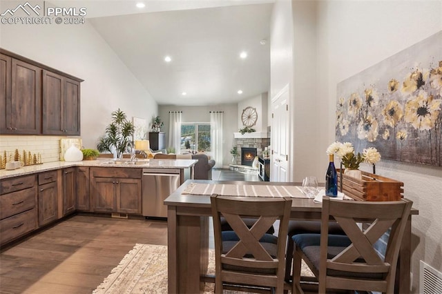 kitchen with backsplash, a stone fireplace, stainless steel dishwasher, dark hardwood / wood-style flooring, and kitchen peninsula