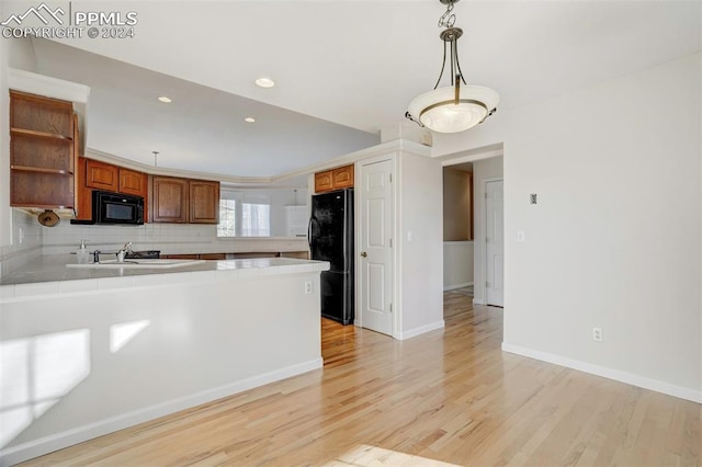 kitchen featuring sink, black appliances, light hardwood / wood-style flooring, tile counters, and hanging light fixtures