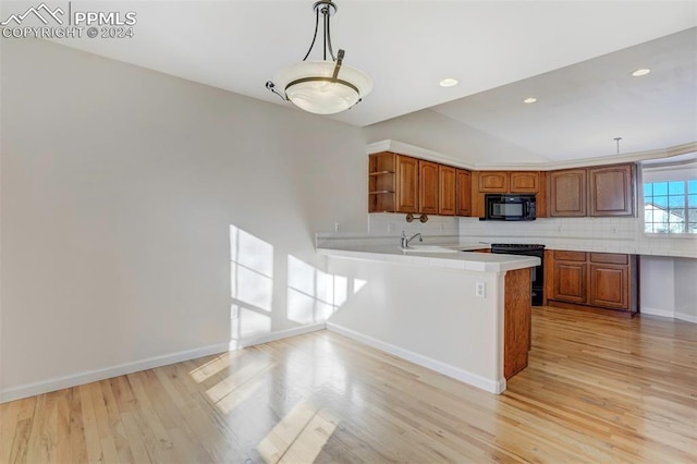 kitchen featuring backsplash, black appliances, light wood-type flooring, decorative light fixtures, and kitchen peninsula