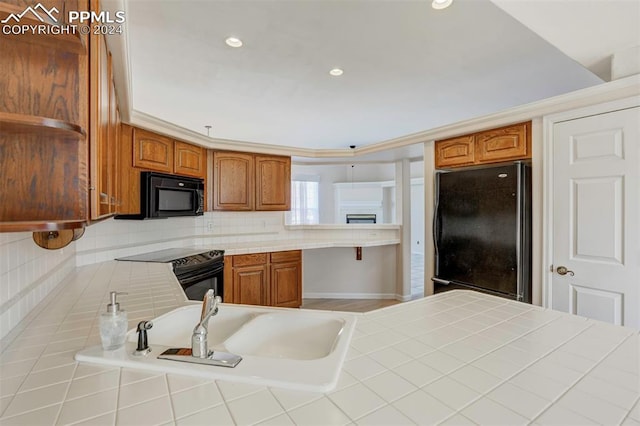 kitchen with tasteful backsplash, tile countertops, crown molding, kitchen peninsula, and black appliances