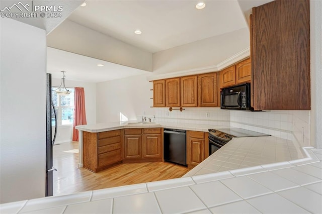 kitchen with kitchen peninsula, light wood-type flooring, sink, black appliances, and tile countertops