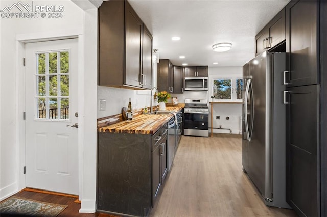 kitchen with butcher block counters, sink, stainless steel appliances, light hardwood / wood-style flooring, and dark brown cabinets