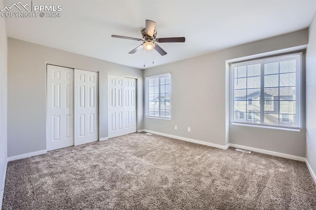 unfurnished bedroom featuring carpet, multiple windows, multiple closets, and ceiling fan