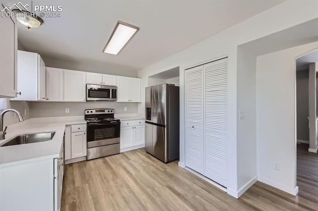 kitchen with sink, white cabinets, light hardwood / wood-style floors, and appliances with stainless steel finishes