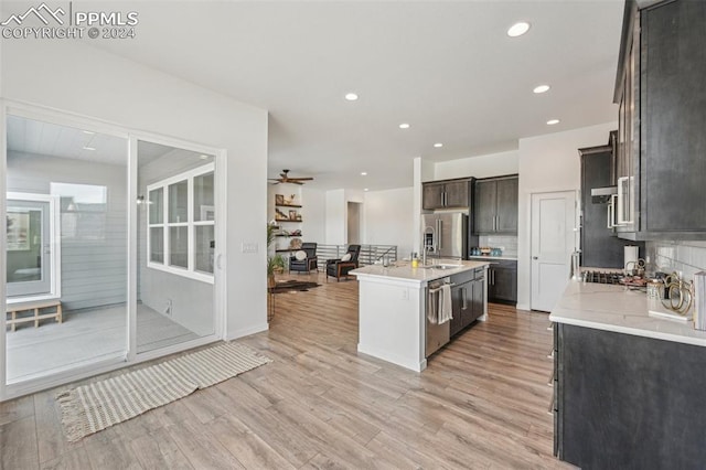 kitchen with light wood-type flooring, tasteful backsplash, dark brown cabinets, stainless steel appliances, and an island with sink