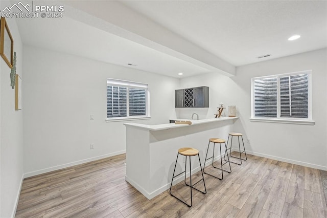 kitchen with kitchen peninsula, light hardwood / wood-style floors, a breakfast bar area, and sink