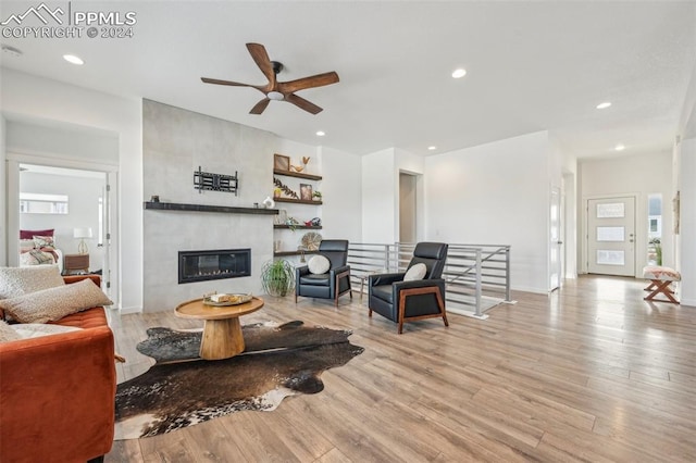 living room featuring a large fireplace, ceiling fan, and light hardwood / wood-style floors