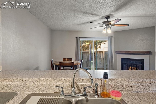 kitchen with ceiling fan, sink, a textured ceiling, and a tile fireplace