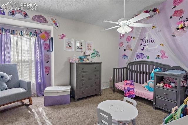 bedroom featuring carpet flooring, a textured ceiling, a nursery area, and ceiling fan