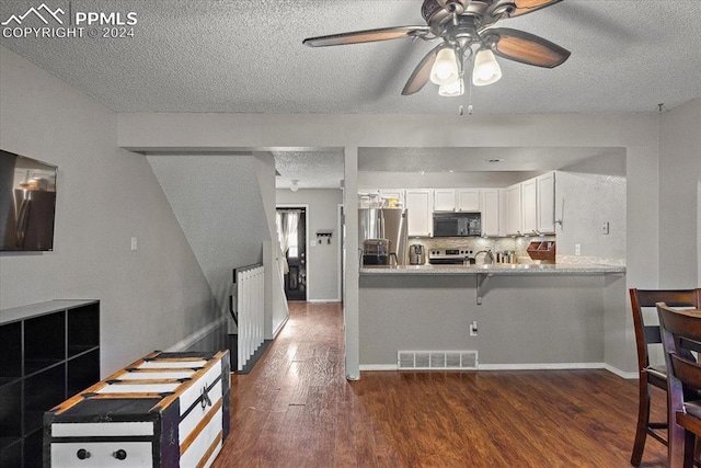 kitchen featuring dark hardwood / wood-style floors, a textured ceiling, white cabinetry, kitchen peninsula, and stainless steel appliances