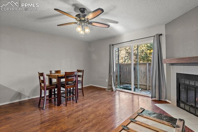 dining room with hardwood / wood-style floors, ceiling fan, a textured ceiling, and a tile fireplace