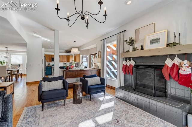 living room with a notable chandelier, a healthy amount of sunlight, light hardwood / wood-style floors, and a tile fireplace