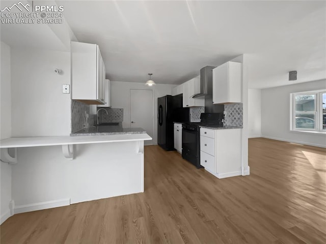 kitchen featuring backsplash, wall chimney exhaust hood, black appliances, wood-type flooring, and white cabinets