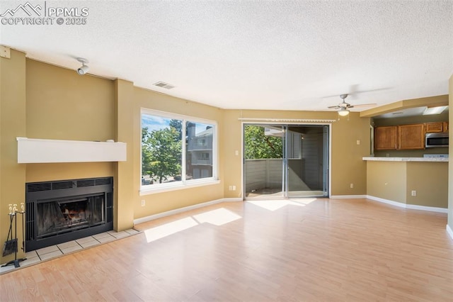 unfurnished living room with a textured ceiling, light hardwood / wood-style flooring, and ceiling fan