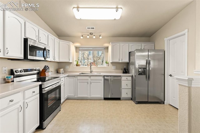 kitchen with white cabinets, sink, appliances with stainless steel finishes, and vaulted ceiling