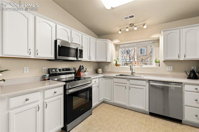 kitchen with white cabinets, stainless steel appliances, vaulted ceiling, and sink