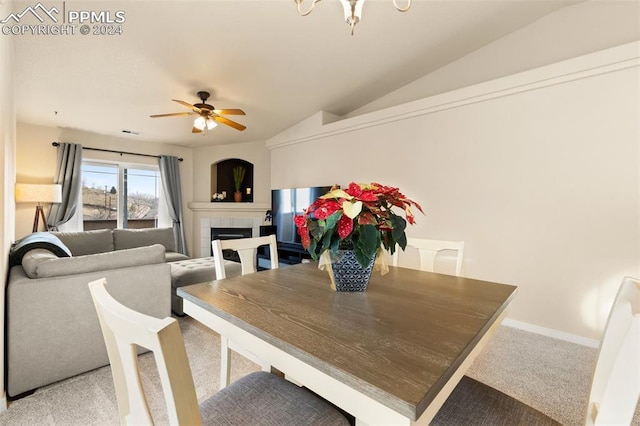 carpeted dining area featuring a tile fireplace, ceiling fan, and lofted ceiling