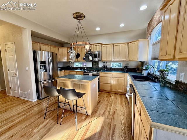 kitchen featuring hanging light fixtures, sink, light hardwood / wood-style floors, appliances with stainless steel finishes, and a kitchen island