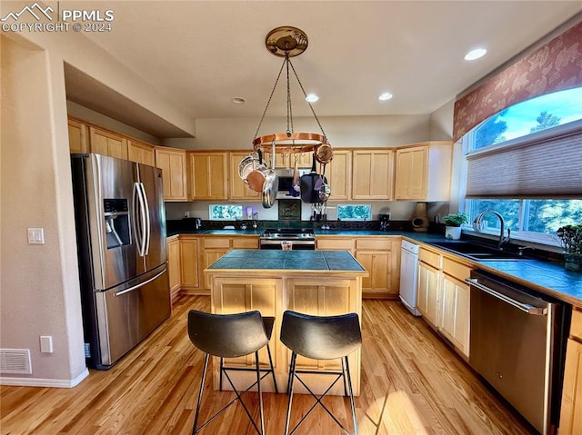 kitchen with appliances with stainless steel finishes, light wood-type flooring, a kitchen breakfast bar, sink, and a center island