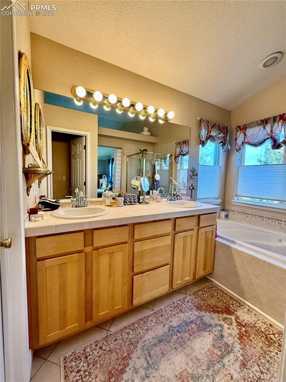 bathroom with tile patterned floors, lofted ceiling, a textured ceiling, vanity, and independent shower and bath