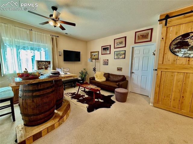 living room featuring wooden walls, ceiling fan, a barn door, a textured ceiling, and carpet floors