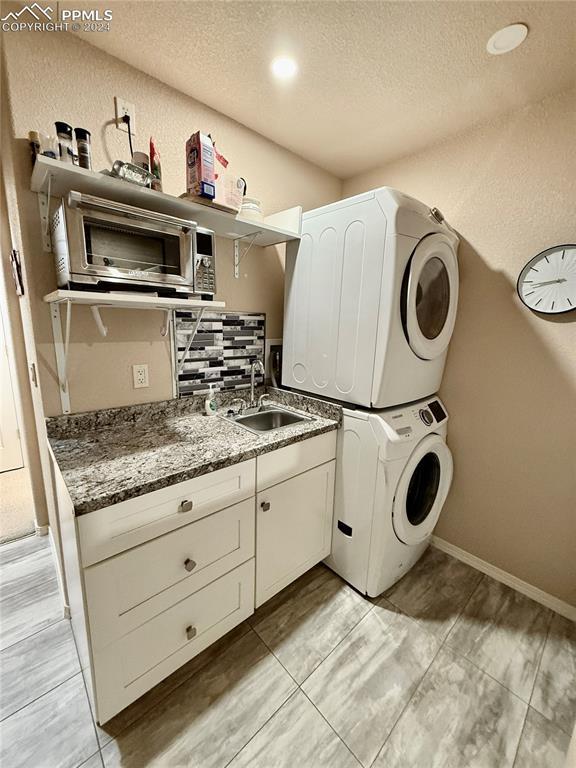 laundry area featuring cabinets, stacked washer and clothes dryer, sink, light tile patterned floors, and a textured ceiling