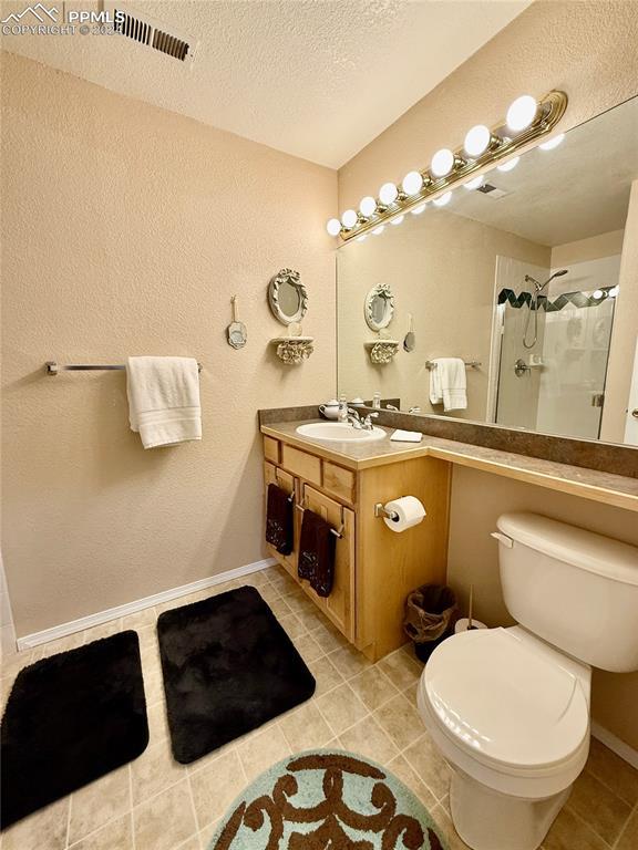 bathroom featuring vanity, tile patterned floors, toilet, a textured ceiling, and walk in shower