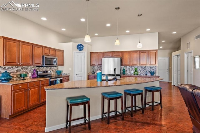 kitchen with a breakfast bar, stainless steel appliances, a kitchen island with sink, and dark wood-type flooring