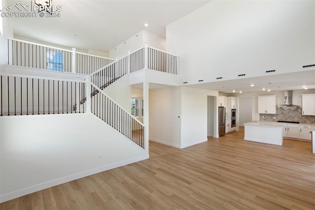 unfurnished living room with light hardwood / wood-style flooring, a towering ceiling, and an inviting chandelier