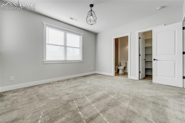 unfurnished bedroom featuring a walk in closet, ensuite bath, and light carpet