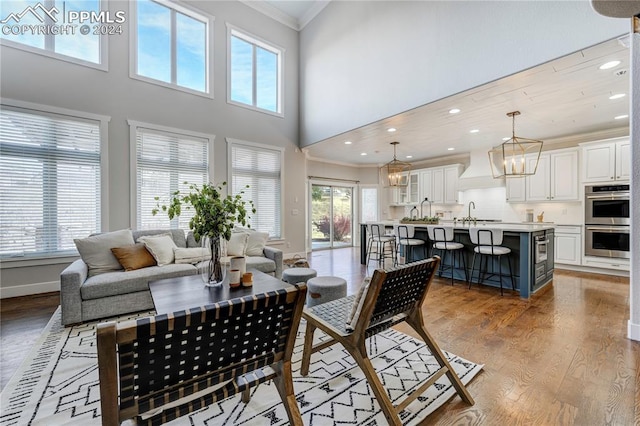 living room with light hardwood / wood-style floors, a high ceiling, a notable chandelier, crown molding, and sink