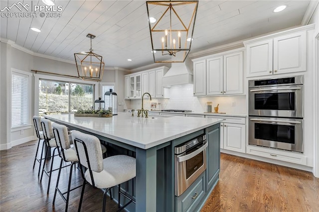 kitchen with appliances with stainless steel finishes, a kitchen island with sink, white cabinets, and custom range hood