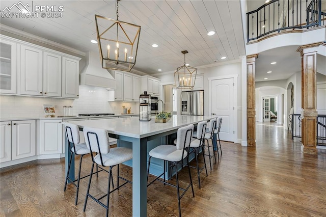 kitchen featuring custom exhaust hood, a center island with sink, a breakfast bar area, dark wood-type flooring, and white cabinets