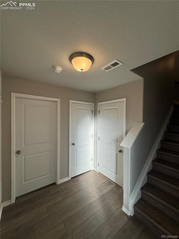 corridor with a textured ceiling and dark wood-type flooring