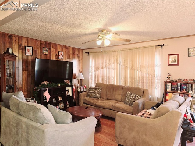 living room featuring a textured ceiling, hardwood / wood-style flooring, ceiling fan, and wooden walls