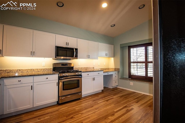 kitchen featuring appliances with stainless steel finishes, light wood-type flooring, light stone counters, vaulted ceiling, and white cabinets