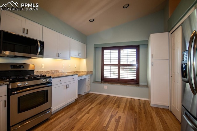 kitchen with lofted ceiling, light wood-type flooring, light stone counters, white cabinetry, and stainless steel appliances