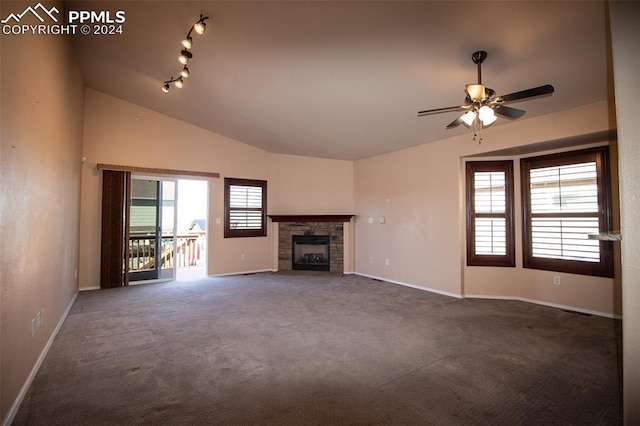 unfurnished living room with dark carpet, lofted ceiling, a stone fireplace, rail lighting, and ceiling fan