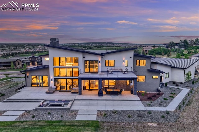 back house at dusk featuring a balcony, a patio, and an outdoor hangout area