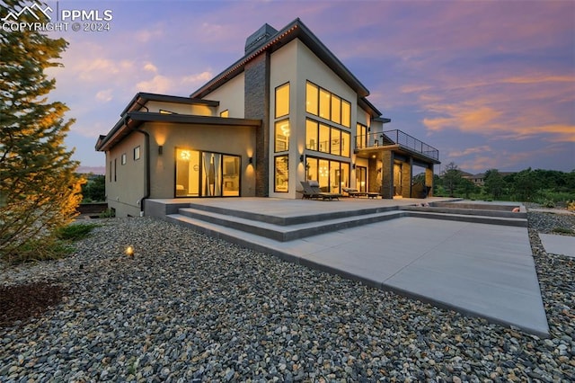 back house at dusk featuring a balcony and a patio area