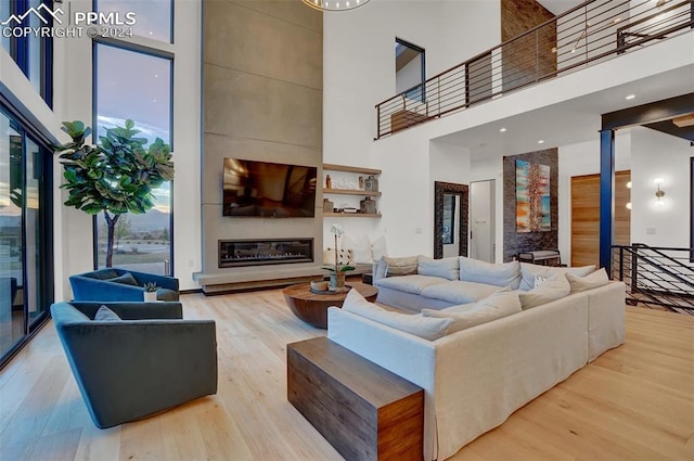 living room featuring a large fireplace, light wood-type flooring, and a towering ceiling