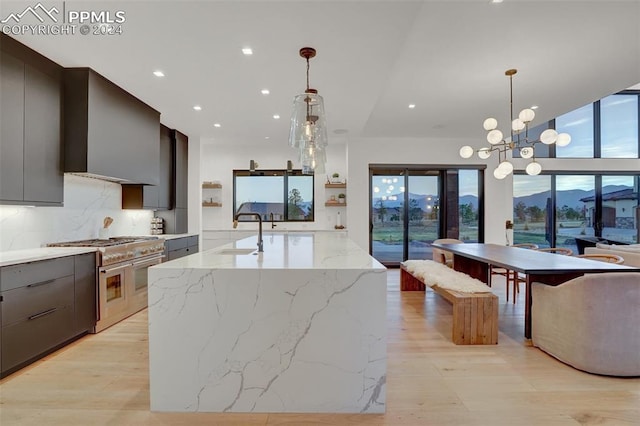 kitchen featuring decorative backsplash, a center island with sink, stainless steel stove, and decorative light fixtures