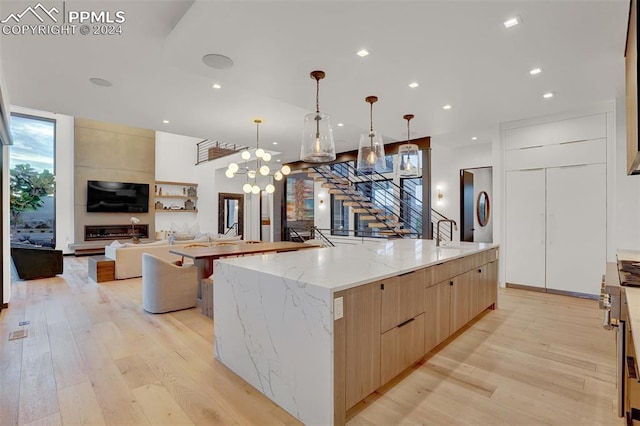 kitchen with hanging light fixtures, a large island, light wood-type flooring, a notable chandelier, and light stone counters