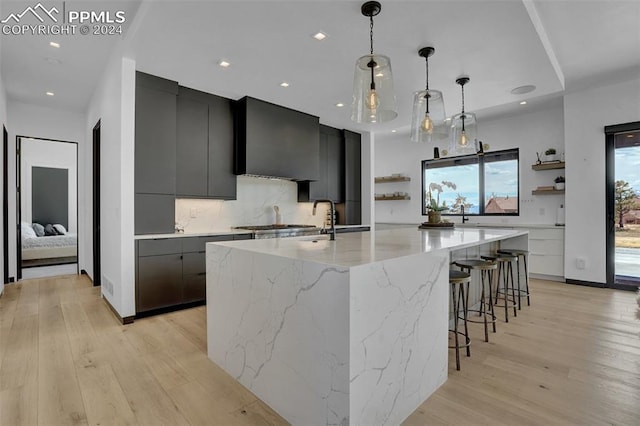 kitchen with backsplash, light hardwood / wood-style floors, a spacious island, and hanging light fixtures