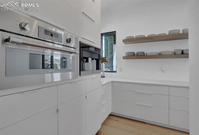 kitchen with oven, white cabinetry, and light hardwood / wood-style floors