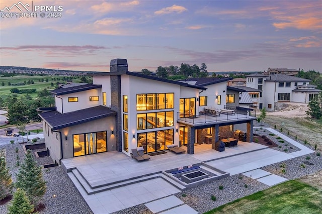 back house at dusk with an outdoor living space, a balcony, and a patio