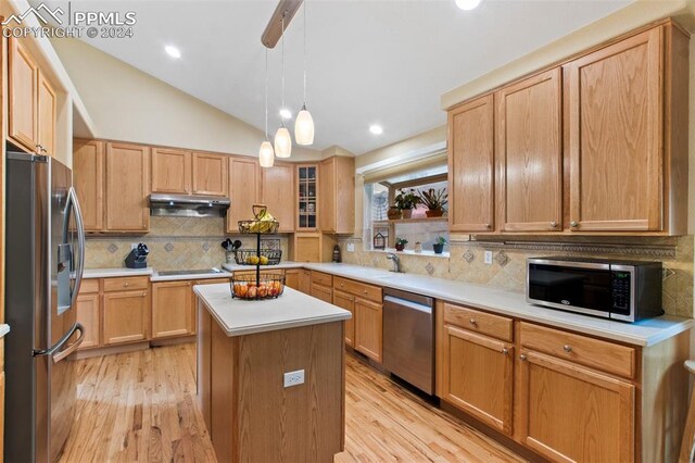 kitchen with appliances with stainless steel finishes, backsplash, vaulted ceiling, light hardwood / wood-style flooring, and a center island